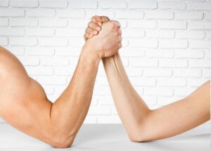Man and woman doing arm wrestling over wall background
