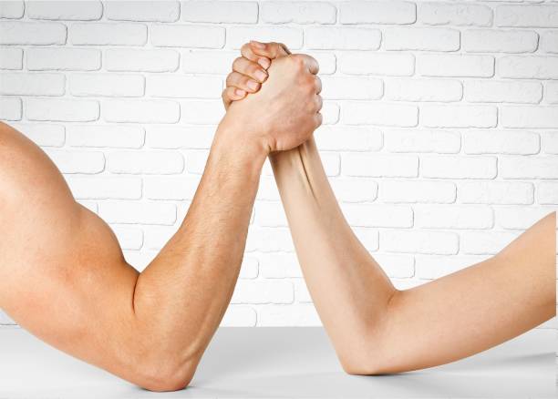 Man and woman doing arm wrestling over wall background