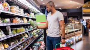 Young african man buying vegetables in grocery section at supermarket. Black man choose vegetables i