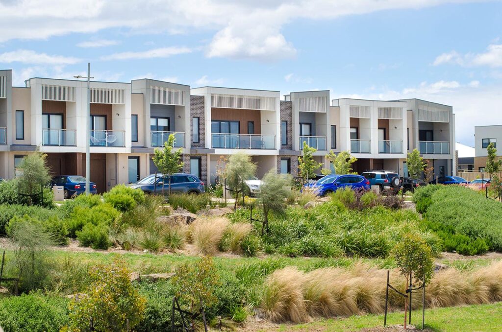 A row of residential townhouses with family cars parked at the front. Modern Australian homes in a new suburb. Concept of residence, real estate development, housing, population, and home ownership.