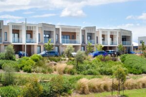 A row of residential townhouses with family cars parked at the front. Modern Australian homes in a new suburb. Concept of residence, real estate development, housing, population, and home ownership.